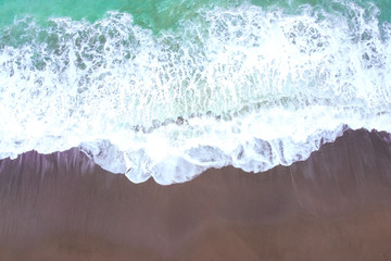 Turquoise foaming sea or ocean wave rolls onto a sandy shore. The top view from a height. Light storm in windy weather. Beautiful and calming seascape for wallpaper. Travel and vacation concept.
