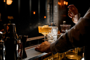 barman actively spray on cold brown alcoholic drink on bar counter.