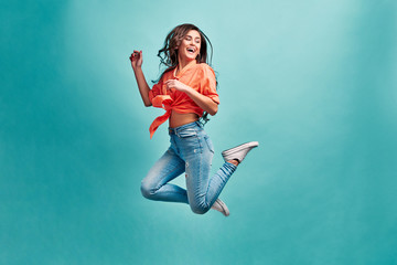 Photo of a beautiful girl bouncing on a blue background with happiness and looking away. The...