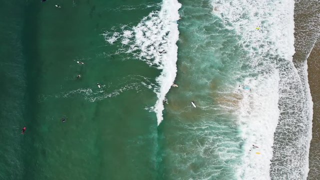 Surfers from above in Praia da Arrifana in west Portugal Atlantic coast, Aerial top view lowering rotating shot