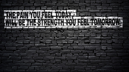the pain you feel today, will be the strength you feel tomorrow, motivation and inspiration slogan, white text on black brick wall
