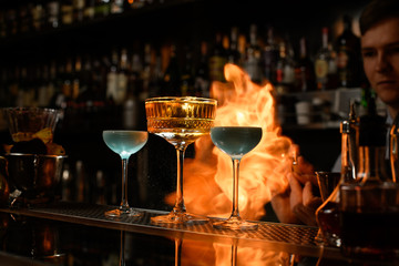 Several wineglasses stands at bar and bartender spraying and sets fire.