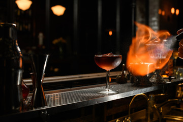 Wineglass stands at bar and bartender spraying and sets fire.