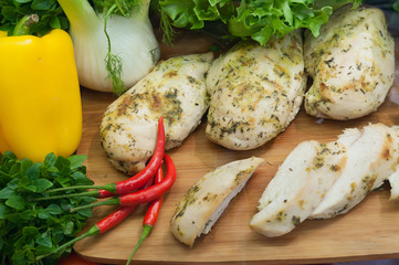 Boiled chicken breast with fresh vegetables and herbs on wooden board on showcase buffet restaurant.