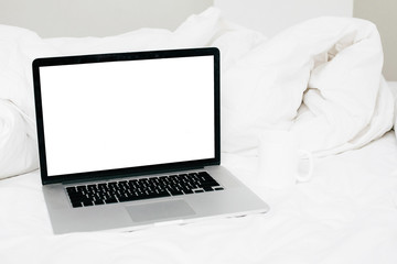 Fototapeta premium Working online from home mockup. Laptop with blank white screen and coffee cup on white cozy bed, copy space. Shopping online from bed. Freelance concept. Staying home. Blog template