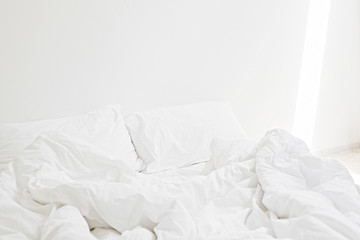 Cozy white bed in the morning. White sheets and pillow on bed in modern white room. Lazy days. Stay home. Comfortable place. Relax on weekend in hotel room. Messy bed