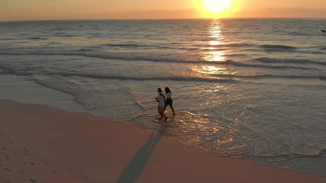 Couple walking on the beach during sunrise aerial side view