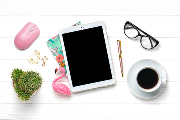 Home office workspace. Tablet, calculator, notepad, golden pen and clips, glasses, flamingo figurine, cup of coffee, succulent, pc mouse on white wooden background. Top view Mock up Flat lay