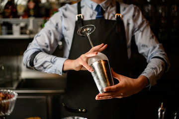 Barman preparing glass and shaker to make cocktail.