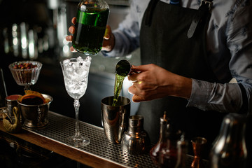 Professional barman using beaker pours drink into shaker