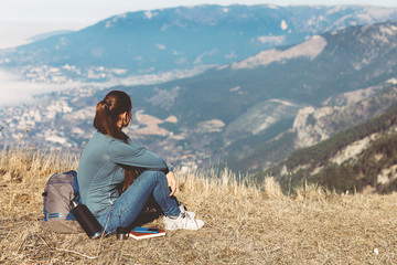 Young beautiful girl travels alone in the mountains in spring or autumn, sits on the edge of the mountain and looks into the distance and enjoys nature, rocks and green forests, view of the landscape