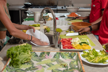 At the large kitchen table, people wash and cook vegetables.