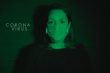 White Adult Woman wearing medical mask looking scared and afraid of coronavirus threat in black background and green light with glitch effect. Text Coronavirus on background.