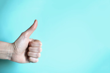 Gesture thumbs up on the plain blue background from the left side
