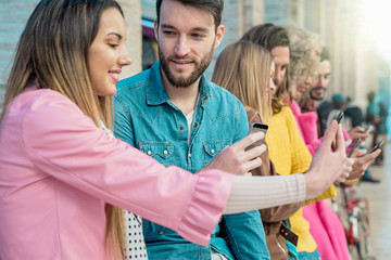 Group of young friends talking and using smart mobile phones. Millennial generation addiction to new technology trends - concept of youth and social media app addiction.