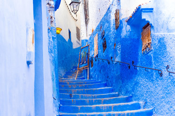 Easel with a picture on the street with stairway in Chefchaouen, blue town Morocco.