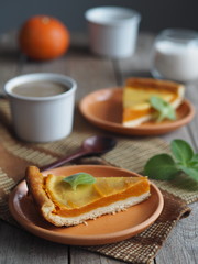 Homemade pumpkin pie covered in whipped eggs with cream and sugar, and a Cup of coffee on a wooden rustic background.Close up.