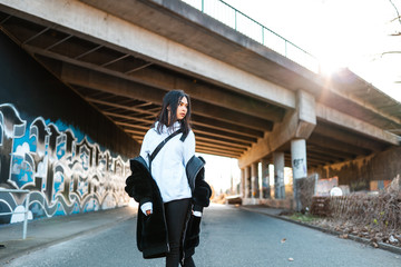 Young women posing in fur coat. In front of bridge with graffiti