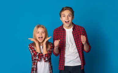Little Brother And Sister Cheering With Raised Hands Over Blue Background