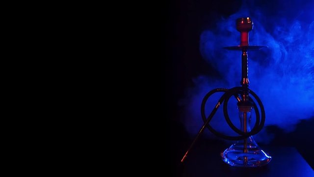hookah with a glass flask with hot coals in a bowl on the table with blue smoke