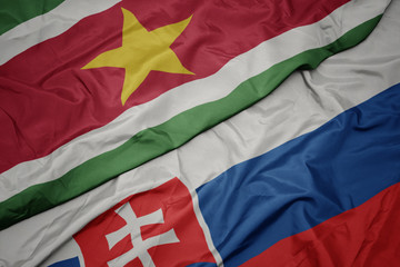 waving colorful flag of slovakia and national flag of suriname.
