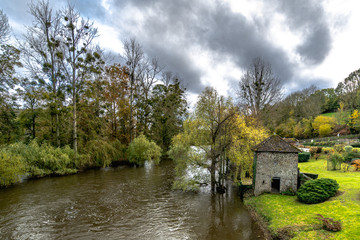 Obraz premium Beautiful stone house covered by lush vegetation near an old stone bridge in a autumnal scenery