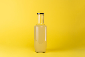 Glass Bottle of lemon juice. Isolated on yellow background