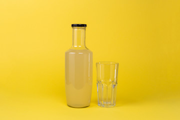Bottle with lemon juice and a glass empty glass next to it is isolated on a yellow background
