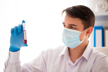 Test tube in male hand, doctor in medical mask holding vial with red liquid. Concept blood sample,...