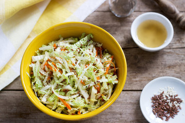 Coleslaw of cabbage, carrots and various herbs with mayonnaise in a large plate on a wooden background.