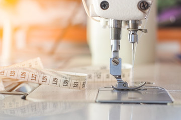 Needle presser foot with blue thread of white industrial sewing machine use sew cloth and tape measure with orange light close-up.
