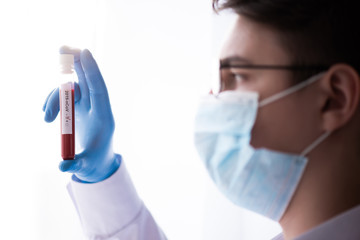 Test tube in male hand close up, doctor in medical mask holding vial with red liquid. Concept blood sample, coronavirus diagnostic, medical research