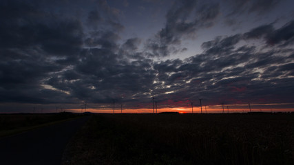 Naklejka na ściany i meble Photo of a colorful sunset over a windmill farm.