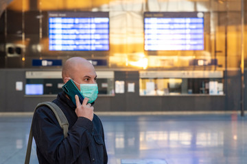 Man in face mask while coronavirus and pandemic in the city and in public transport. Man using phone on railway station and protect health while covid19.