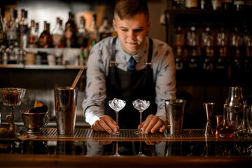 bartender holds two glasses with ice on bar counter.