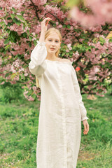 Gorgeous female model having fun in blooming garden. Natural background with blossom, warm sunlight, wellness and fitness concept. Sensual blond girl in white linen dress walking in Paris streets.