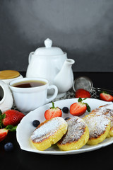 Gourmet Breakfast - Cottage cheese pancakes, syrniki with powdered sugar and fresh berries on a white plate, tea. 