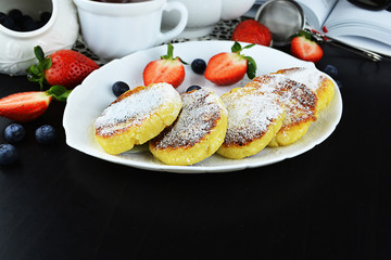 Fried cottage cheese pancakes or syrniki served with strawberries, blackberries and cup of coffee. Traditional breakfast of Ukrainian and Russian cuisine, space for text