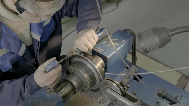 A skilled worker in blue measures the dimensions of a part using a vernier caliper at the factory.