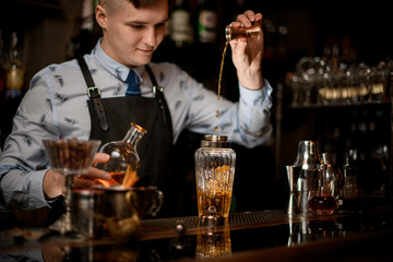young bartender at bar pours drink into shaker using beaker