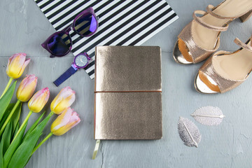 A gold notebook with women's shoes, tulips, glasses and a watch on a concrete background. Flet lay © Вася Фаевич