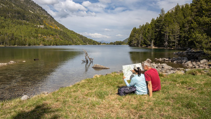 Beautiful Pyrenees mountain landscape, nice lake with tourist couple looking a map. Spain, Catalonia.