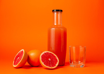 Grapefruit juice glass bottle. Isolated. Bottle with grapefruit juice and an empty glass, whole and cut fruits on an orange background. Healthy eating concept. Minimalism