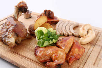 Dish of assorted meat. Big tasty baked  knuckle, homemade sausages, grilled bird, potatoes. With greens and sauces. On a wooden board.
