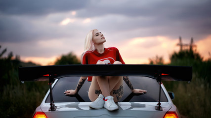 Beautiful blonde is sitting on a car
