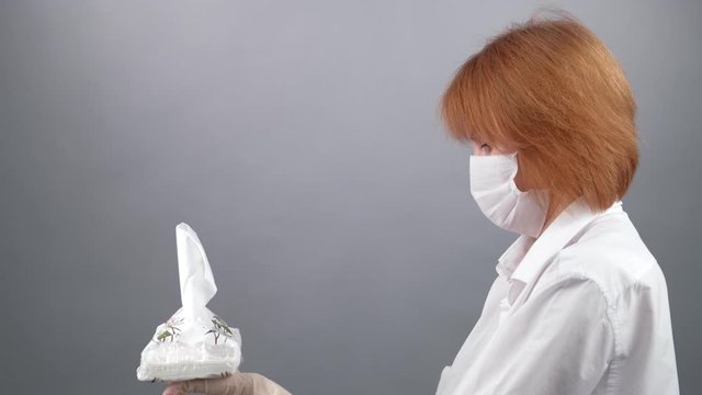 Woman wearing medical mask and gloves take out paper napkin from dispenser box at grey background, closeup shot. 2019 Novel Coronavirus 2019-nCoV, COVID-19 concept.