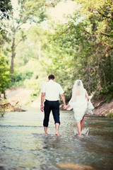Wedding concept. Bride and groom holding hands and fording the river. Happy newlyweds