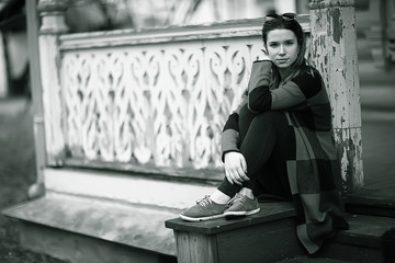 girl is sitting on a garden bench / beautiful model posing sitting in  coat on  bench in  city park, beautiful girl