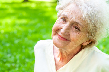 Pretty happy elderly woman on a background of spring greenery close-up with a smile on her face. The health of old people. Retirement Care - obrazy, fototapety, plakaty