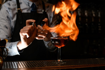 bartender makes fire over glass with cocktail